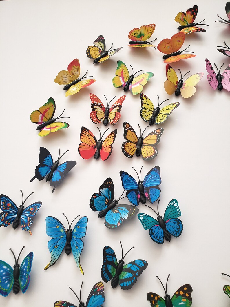 May include: A collection of colorful butterfly decorations in various sizes and designs. The butterflies feature shades of yellow, orange, red, pink, and blue. Each butterfly has a black body and antenna, creating a vibrant and eye-catching display.
