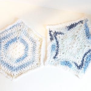 May include: Two handmade crochet items in shades of white and blue. One is a hexagon shape with concentric rings of color. The other is a star shape with blue accents. Both items have a soft, textured appearance.