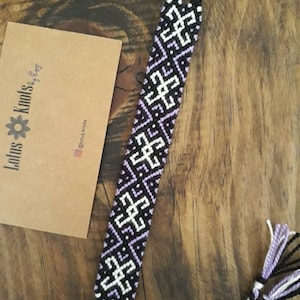 Peut inclure: Un bracelet d'amitié noir et violet avec un motif géométrique. Le bracelet est noué à l'extrémité.