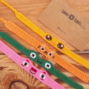 May include: Four colorful friendship bracelets with different cartoon faces. The bracelets are made with colorful embroidery floss and feature a variety of expressions, including a smiling face, a winking face, and a surprised face. The bracelets are arranged in a row on a wooden surface. The text "Lotus Knots by Egg" is visible on a brown card in the background.