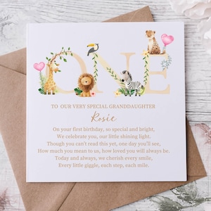May include: A light purple card with the word "ONE" in large, gold letters decorated with jungle animals. The text "To our very special granddaughter Rosie" is written in gold script. The card reads "On your first birthday, so special and bright, We celebrate you, our little shining light. Though you can't read this yet, one day you'll see, How much you mean to us, how loved you will always be. Today and always, we cherish every smile, Every little giggle, each step, each mile."