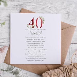 May include: A square white greeting card featuring the red number 40 decorated with floral illustrations, the text Happy Ruby Anniversary to my Husband John, and a printed poem about love, resting on a brown paper envelope.