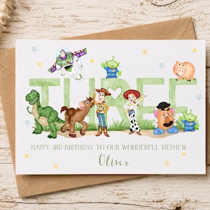 May include: A white birthday greeting card featuring the word THREE in large green letters, decorated with illustrations of Buzz Lightyear, Rex, Bullseye, Woody, Jessie, Mr. Potato Head, and two aliens. Text reads: HAPPY 3RD BIRTHDAY TO OUR WONDERFUL NEPHEW Oliver.