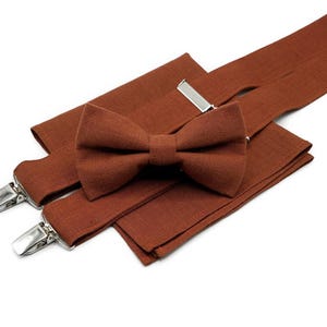 Puede incluir: Un conjunto de tirantes de lino marrón y una pajarita a juego. Los tirantes tienen clips plateados y la pajarita está atada.