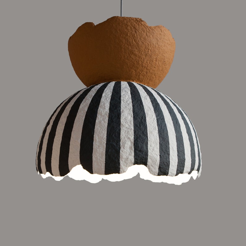 May include: A black and white striped paper lampshade with a brown paper top. The lampshade is hanging from the ceiling.