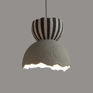 May include: A hanging light fixture with a white and black striped top and a cracked, light green bottom. The light is on and illuminates the bottom of the fixture.