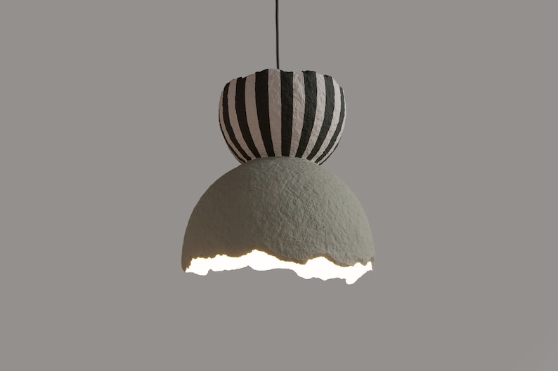 May include: A hanging light fixture with a white and black striped top and a cracked, light green bottom. The light is on and illuminates the bottom of the fixture.