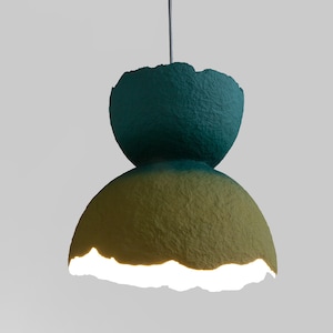 May include: A teal and yellow paper lampshade with a unique, textured, and slightly irregular shape. The lampshade is lit from within, casting a warm glow.