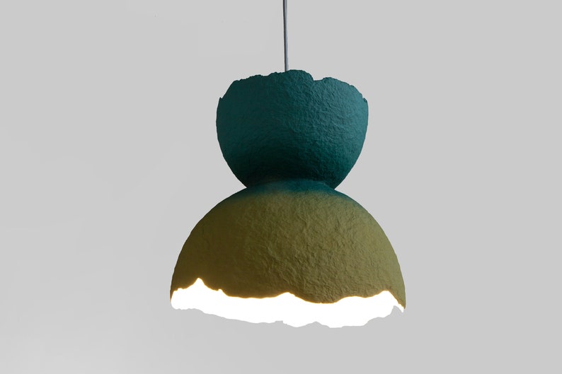 May include: A teal and yellow paper lampshade with a unique, textured, and slightly irregular shape. The lampshade is lit from within, casting a warm glow.