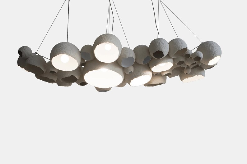May include: A white paper pendant light fixture with multiple round shades of varying sizes. The shades are suspended from the ceiling by thin wires and are arranged in a cluster.