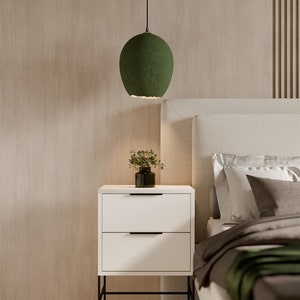K&ouml;nnte beinhalten: Ein Schlafzimmer mit einem wei&szlig;en Bettgestell, einem gr&uuml;nen Lampenschirm und einem wei&szlig;en Nachttisch mit zwei Schubladen. Die W&auml;nde sind in hellem Holzton gehalten.