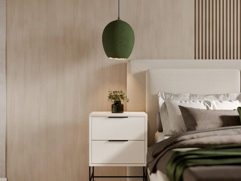 K&ouml;nnte beinhalten: Ein Schlafzimmer mit einem wei&szlig;en Bettgestell, einem gr&uuml;nen Lampenschirm und einem wei&szlig;en Nachttisch mit zwei Schubladen. Die W&auml;nde sind in hellem Holzton gehalten.