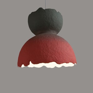 May include: A red and gray paper lampshade with a unique, textured, and slightly irregular shape. The lampshade has a white interior and is hanging from a cord.