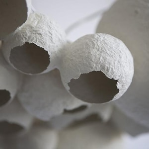 May include: A close-up of a white paper mache sculpture with a textured surface and several holes. The sculpture is made of multiple spheres that are connected together.