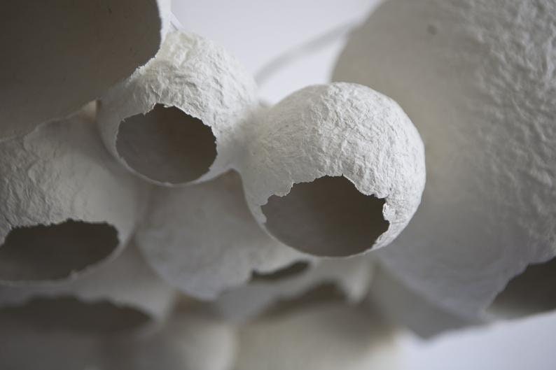 May include: A close-up of a white paper mache sculpture with a textured surface and several holes. The sculpture is made of multiple spheres that are connected together.