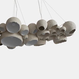 May include: A white paper pendant light fixture with multiple round shades of varying sizes. The shades are suspended from the ceiling by thin wires.