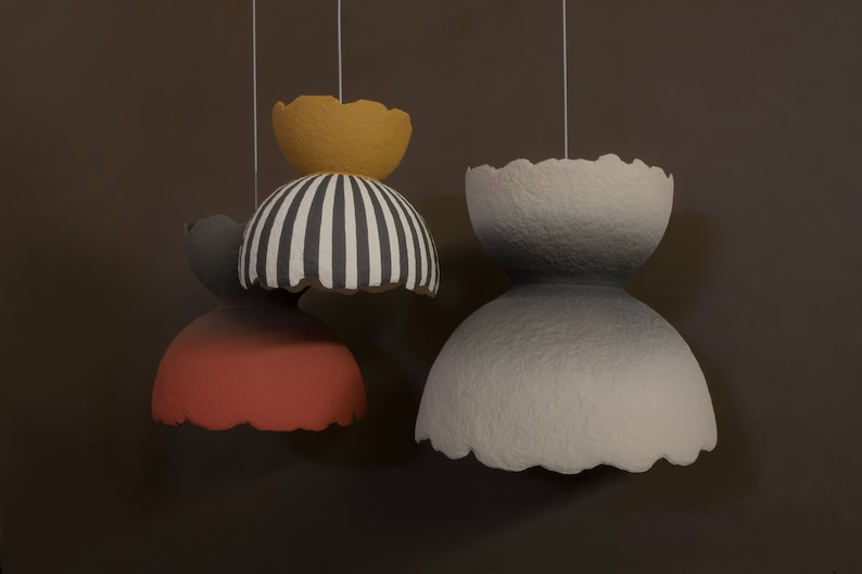 May include: Three hanging paper lampshades. The top lampshade is yellow, the middle lampshade is black and white striped, and the bottom lampshade is red.