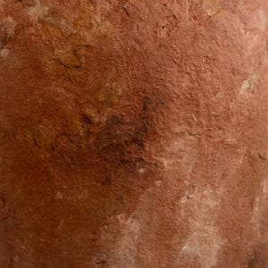 Op de afbeelding: Close-up van een terracotta-gekleurde, getextureerde vaas. Het oppervlak heeft een ruwe, ongelijke uitstraling met kleurvariaties, vari&euml;rend van lichtbruin tot diep bruin. De vaas lijkt handgemaakt te zijn, met zichtbare onvolkomenheden.