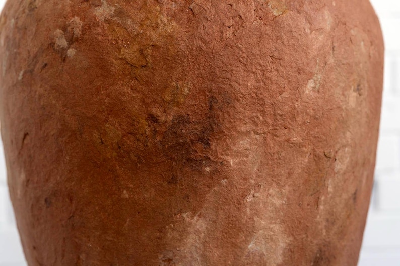 Op de afbeelding: Close-up van een terracotta-gekleurde, getextureerde vaas. Het oppervlak heeft een ruwe, ongelijke uitstraling met kleurvariaties, vari&euml;rend van lichtbruin tot diep bruin. De vaas lijkt handgemaakt te zijn, met zichtbare onvolkomenheden.