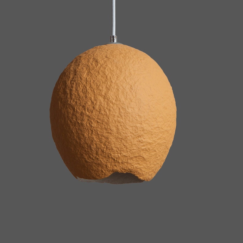 K&ouml;nnte beinhalten: Eine runde, orangefarbene, strukturierte Pendelleuchte mit einem wei&szlig;en Kabel.