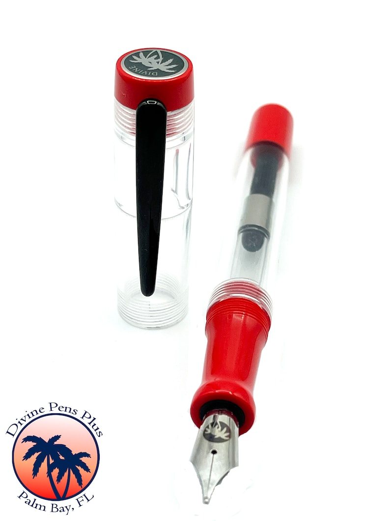May include: A clear fountain pen with red accents and a silver nib. The pen's cap is red with a silver emblem and the text "DIVINE". The pen is displayed on a white background. The pen is from Divine Pens Plus, Palm Bay, FL.