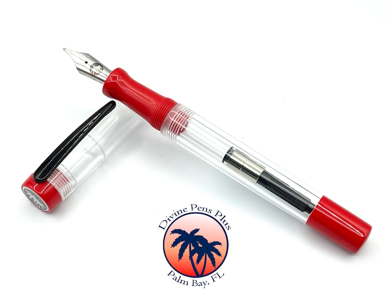 May include: A clear fountain pen with a red grip and accents, and a silver nib. The pen's cap is off and next to the pen. The pen has a clear barrel, revealing the ink reservoir. The pen is on a white surface.