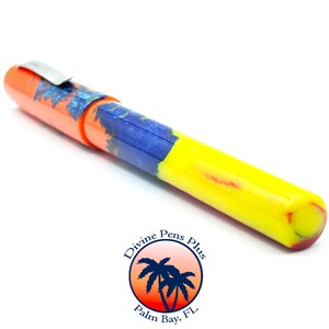 May include: A colorful pen with an orange cap, a blue and orange patterned section, and a yellow barrel. The pen has a silver clip and is set against a white background. The pen is from Divine Pens Plus, Palm Bay, FL.