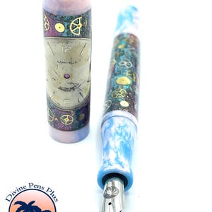 Puede incluir: Una pluma estilogr&aacute;fica con dise&ntilde;o steampunk. La pluma presenta un cuerpo y capuch&oacute;n veteados en azul y blanco, con engranajes dorados y un dise&ntilde;o de esfera de reloj. La pluma es de Divine Pens Plus, Palm Bay, FL.