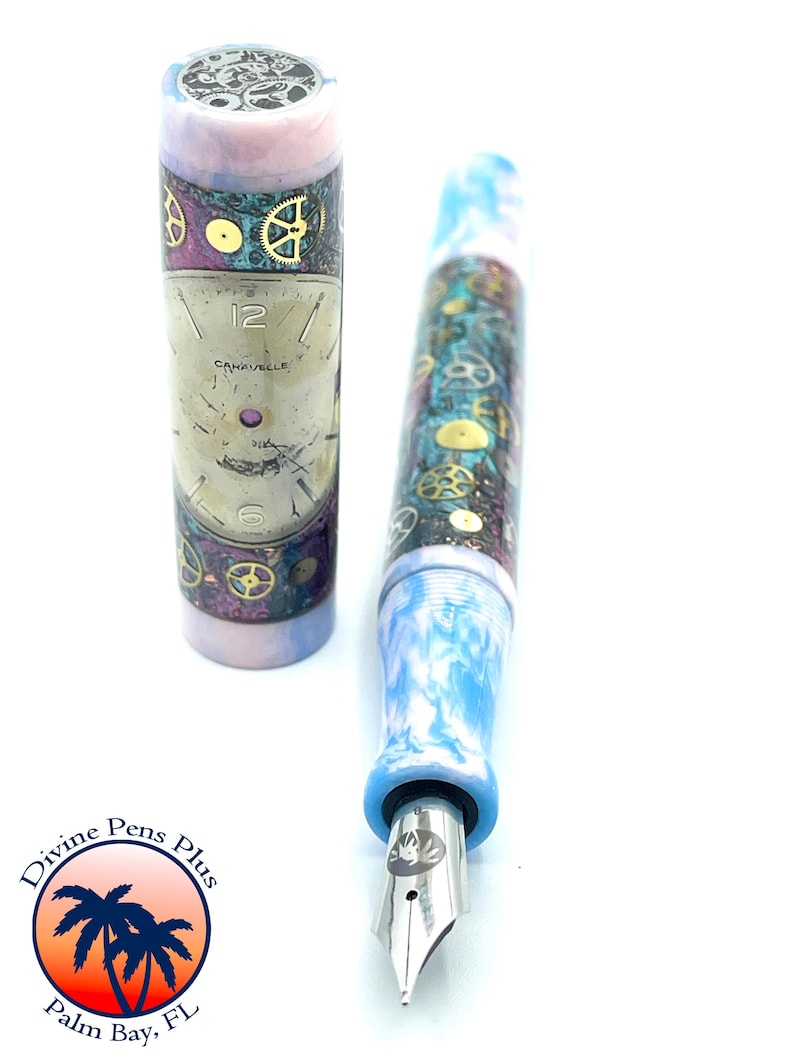 Puede incluir: Una pluma estilogr&aacute;fica con dise&ntilde;o steampunk. La pluma presenta un cuerpo y capuch&oacute;n veteados en azul y blanco, con engranajes dorados y un dise&ntilde;o de esfera de reloj. La pluma es de Divine Pens Plus, Palm Bay, FL.