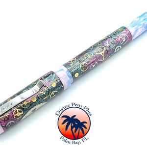 Puede incluir: Pluma estilogr&aacute;fica detallada con dise&ntilde;o steampunk. La pluma presenta un clip met&aacute;lico y un cuerpo adornado con engranajes en oro, plata y bronce. Los extremos de la pluma tienen un patr&oacute;n veteado azul y blanco. La pluma tiene la palabra "Divine" en el clip.