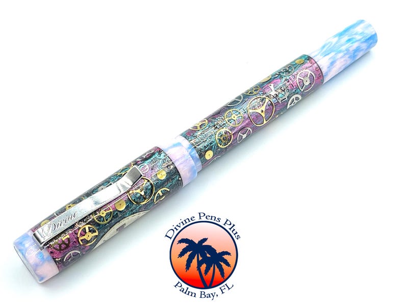 Puede incluir: Pluma estilogr&aacute;fica detallada con dise&ntilde;o steampunk. La pluma presenta un clip met&aacute;lico y un cuerpo adornado con engranajes en oro, plata y bronce. Los extremos de la pluma tienen un patr&oacute;n veteado azul y blanco. La pluma tiene la palabra "Divine" en el clip.