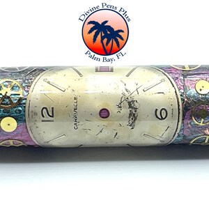 Puede incluir: Un bol&iacute;grafo con un dise&ntilde;o de esfera de reloj vintage. El bol&iacute;grafo presenta una esfera de reloj color crema con los n&uacute;meros 12 y 6 visibles. El cuerpo del bol&iacute;grafo tiene un dise&ntilde;o de inspiraci&oacute;n steampunk con engranajes y una mezcla de colores p&uacute;rpura, verde azulado y plateado.