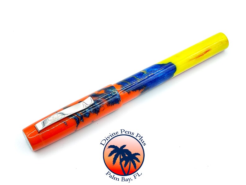 May include: A colorful pen with a vibrant design. The pen features a bright orange, blue, and yellow pattern. It has a silver clip and the text "Prestige" is visible. The pen is a writing instrument.