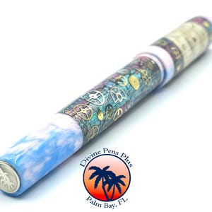 Puede incluir: Un bol&iacute;grafo &uacute;nico con un cuerpo veteado azul y blanco, que se transforma en una secci&oacute;n adornada con engranajes y dise&ntilde;os de relojer&iacute;a. El bol&iacute;grafo presenta una punta plateada y un logotipo que dice "Divine Pens Plus, Palm Bay, FL."