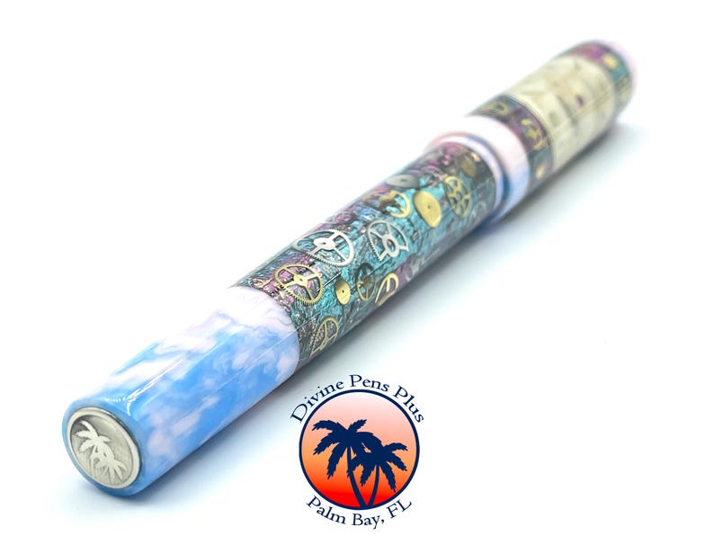 Puede incluir: Un bol&iacute;grafo &uacute;nico con un cuerpo veteado azul y blanco, que se transforma en una secci&oacute;n adornada con engranajes y dise&ntilde;os de relojer&iacute;a. El bol&iacute;grafo presenta una punta plateada y un logotipo que dice "Divine Pens Plus, Palm Bay, FL."
