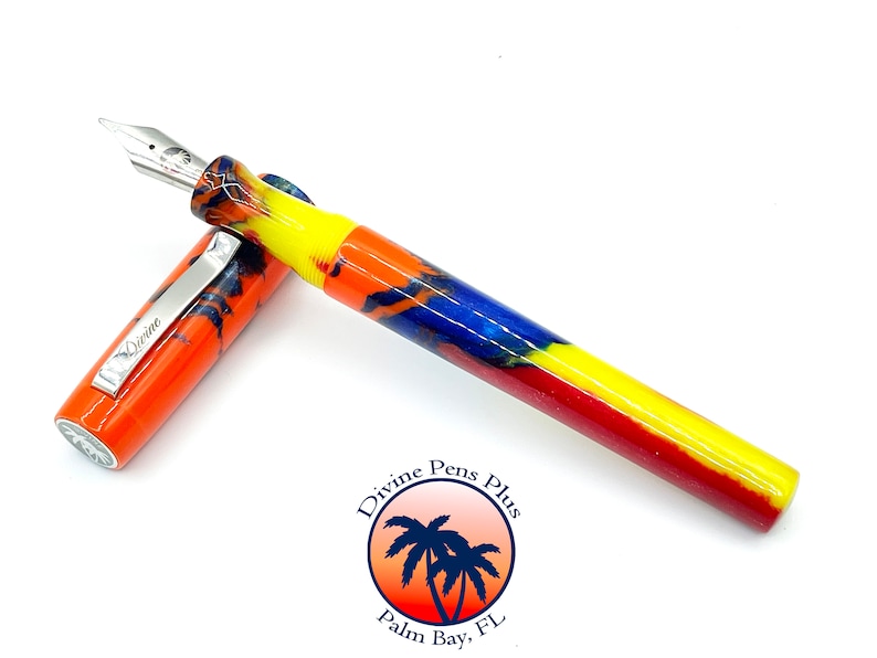May include: A colorful fountain pen with a silver nib and clip. The pen's body features a vibrant pattern of orange, yellow, blue, and red. The clip is engraved with the word "Divine". The pen is from Divine Pens Plus, Palm Bay, FL.