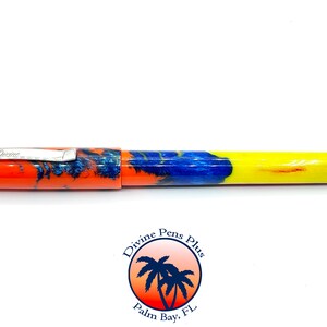 May include: A colorful pen with a vibrant design. The pen features an orange cap and barrel, transitioning to blue and yellow. The pen has a silver clip with the word "Divine" engraved on it. The pen is a writing instrument.