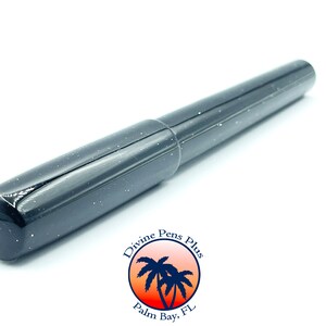 May include: A black fountain pen with a speckled, glittery finish. The pen has a rounded tip and a cap that fits snugly over the nib. The pen is set against a white background. The pen is from Divine Pens Plus, Palm Bay, FL.
