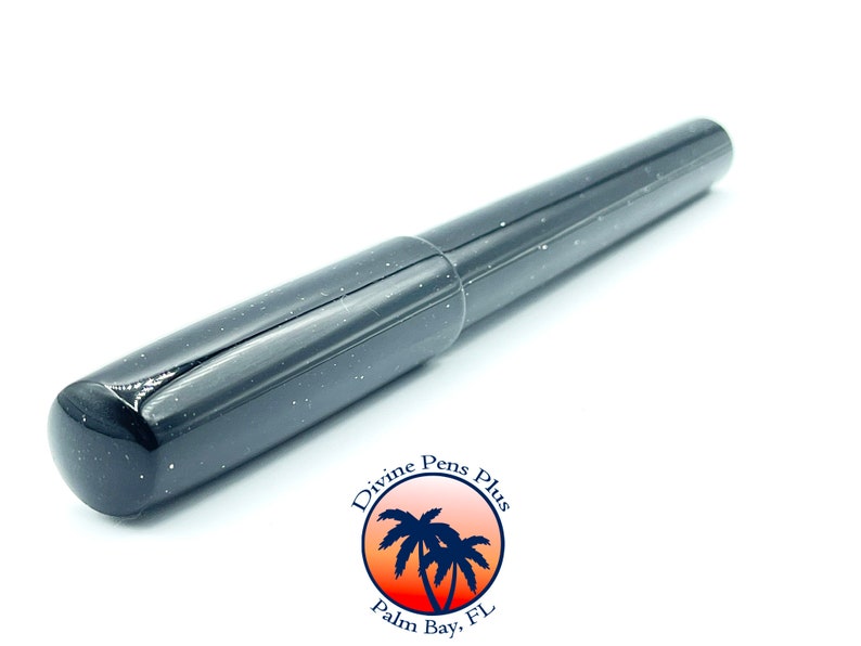 May include: A black fountain pen with a speckled, glittery finish. The pen has a rounded tip and a cap that fits snugly over the nib. The pen is set against a white background. The pen is from Divine Pens Plus, Palm Bay, FL.