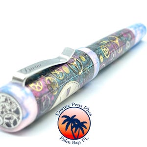 Puede incluir: Una pluma estilogr&aacute;fica con un dise&ntilde;o steampunk. La pluma presenta un clip plateado con la palabra "Divine" y un barril decorado con engranajes y patrones de relojer&iacute;a dorados, morados y turquesas. El extremo de la pluma tiene un dise&ntilde;o de engranaje.