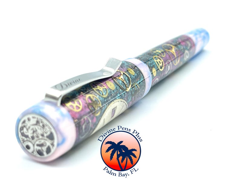 Puede incluir: Una pluma estilogr&aacute;fica con un dise&ntilde;o steampunk. La pluma presenta un clip plateado con la palabra "Divine" y un barril decorado con engranajes y patrones de relojer&iacute;a dorados, morados y turquesas. El extremo de la pluma tiene un dise&ntilde;o de engranaje.