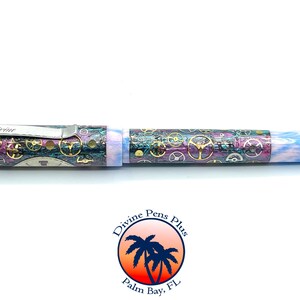 Puede incluir: Pluma detallada con dise&ntilde;o steampunk. La pluma presenta un clip plateado con la palabra "Divine" grabada. El cuerpo est&aacute; decorado con engranajes y una mezcla de colores, incluyendo morado, dorado y azul. El extremo de la pluma tiene un dise&ntilde;o veteado azul y blanco.