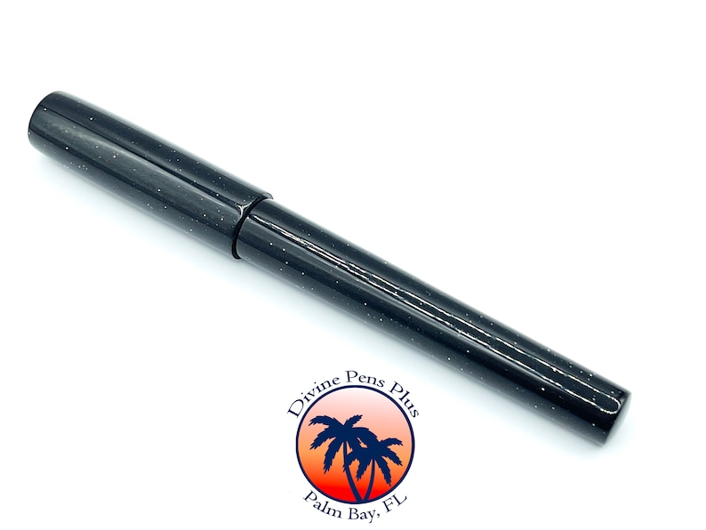 May include: A black fountain pen with a speckled, glittery finish. The pen has a cap and a sleek, modern design. The logo for Divine Pens Plus is visible in the lower right corner.