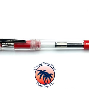 May include: A clear fountain pen with red accents. The pen has a transparent barrel, a black clip, and red ends. The nib is visible, and the pen appears to be new. The pen is a writing instrument.