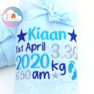 May include: A light blue baby blanket with a white cloud pattern. The blanket is embroidered with the name "Kian", the date "1st April 2020", the time "6:50 am", the weight "3.36 kg", and a star and footprints.
