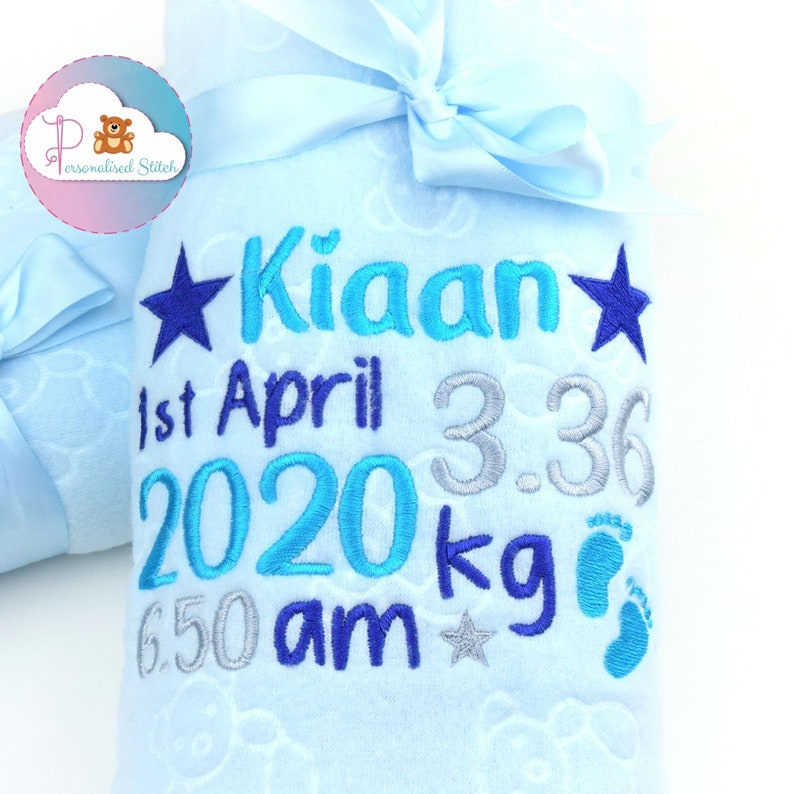 May include: A light blue baby blanket with a white cloud pattern. The blanket is embroidered with the name "Kian", the date "1st April 2020", the time "6:50 am", the weight "3.36 kg", and a star and footprints.