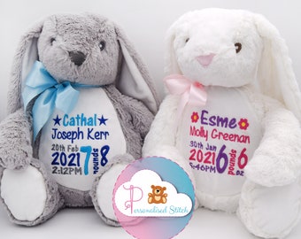 May include: Two plush stuffed bunnies, one grey and one white, featuring embroidered birth details. The grey bunny has a blue ribbon and blue text reading Cathal Joseph Kerr 20th Feb 2021 7 pounds 8 2:12PM. The white bunny has a pink ribbon and pink text reading Esme Molly Greenan 30th Jan 2021 6 pounds 6 5:46PM.