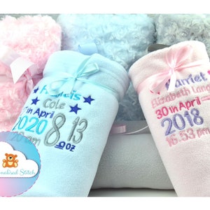 May include: Two personalized baby blankets, one blue and one pink, with embroidered names, birth dates, and times. The blankets are made of soft fleece and have a satin ribbon tied around them.