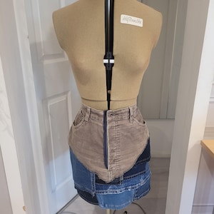 May include: A brown corduroy skirt with a denim patchwork design. The skirt is on a dress form.