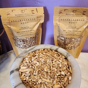 May include: Two brown paper bags filled with dried ashwagandha root. The bags have a label that reads "Ashwagandha Root, Premium Wildcrafted, 85&deg;c | Steep 10-15 minutes, Net Wt: 51.02g / 1.80z, Distributed by Herbalisticwellness.com". A white mortar and pestle contains a pile of the dried root.